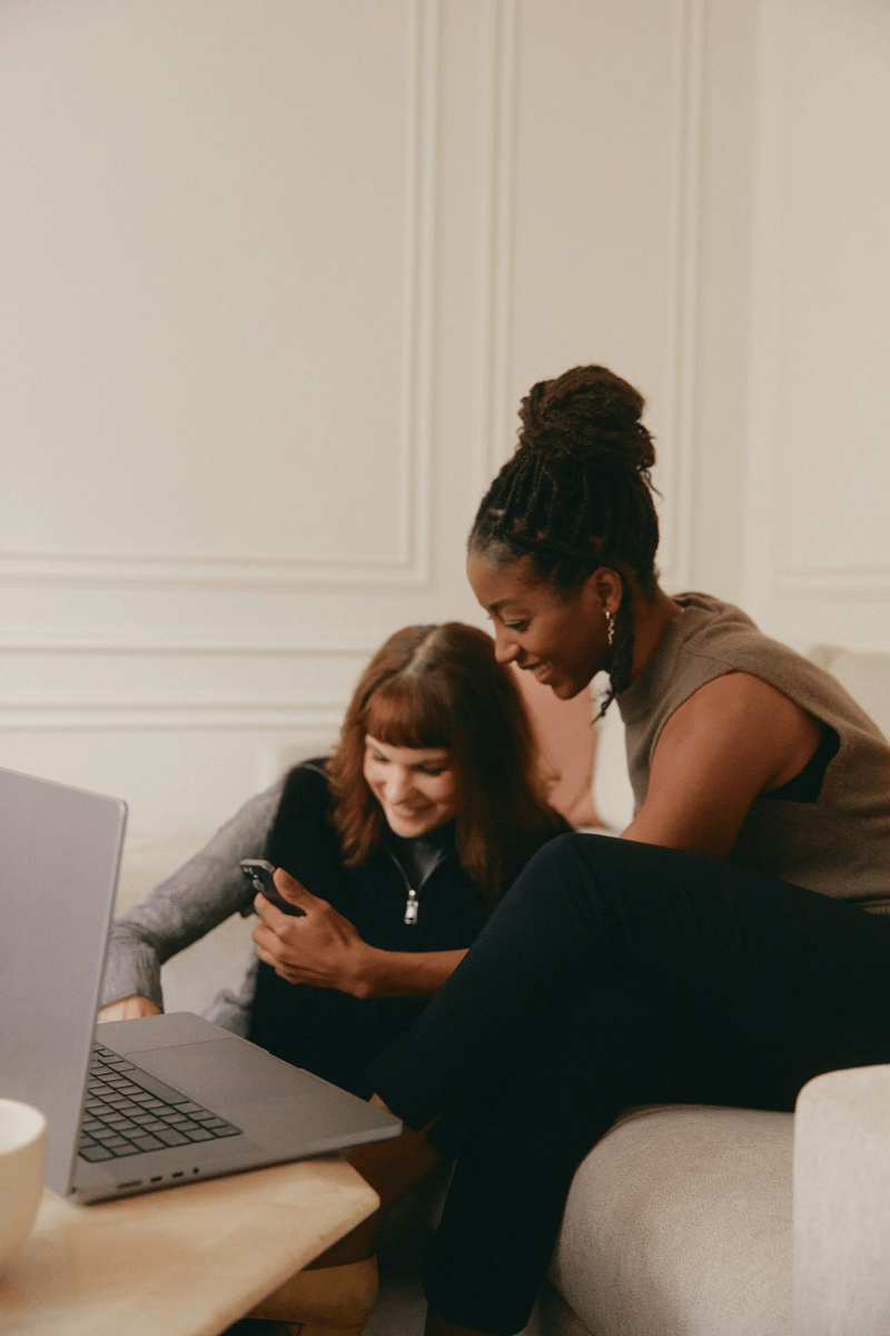Two people sitting on a couch with their electronics